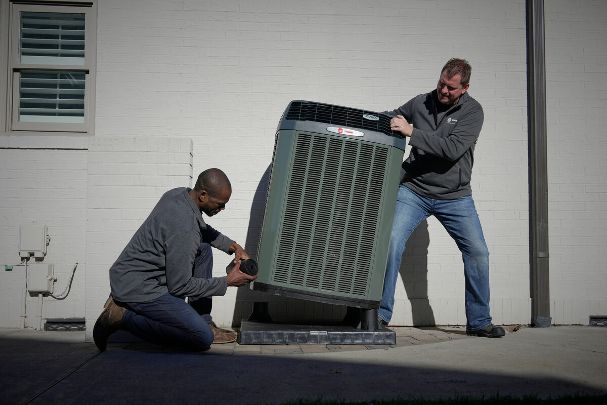 Two HVAC technicians standing beside an outdoor unit during service